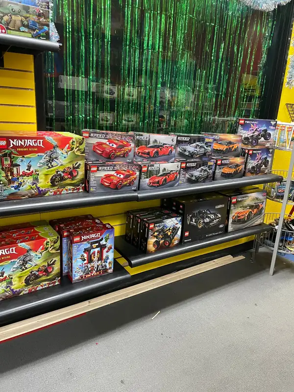 Boxed LEGO® vehicle sets lined up on black shelves against a yellow wall.
