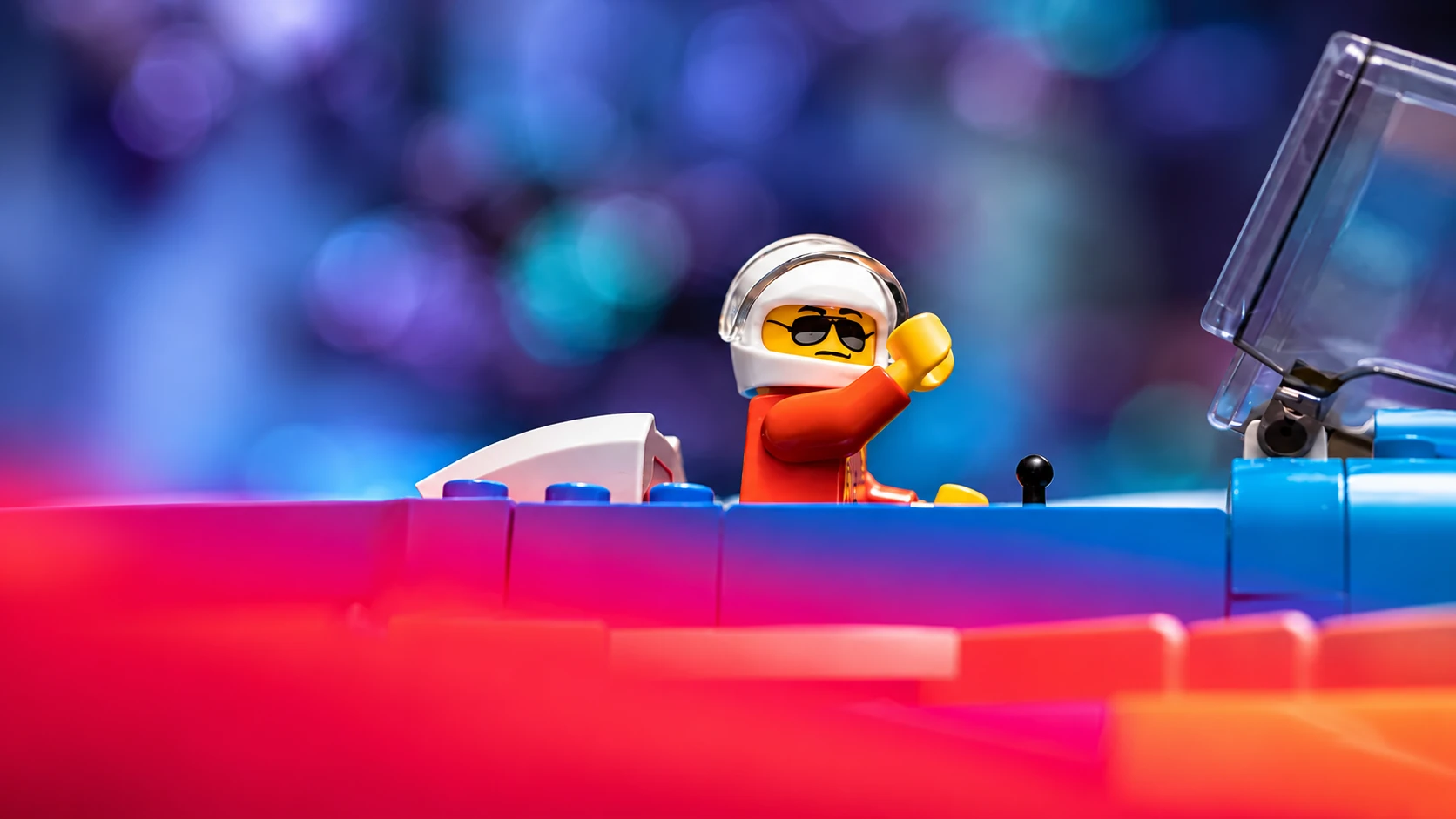 A helmeted LEGO® minifigure driving a red and blue brick-built vehicle.